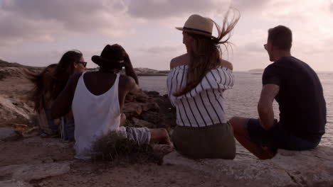 group of friends sit on cliff watching sunset shot on r3d