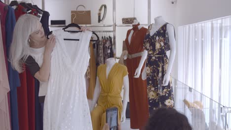 mujer feliz eligiendo ropa en la tienda de moda y su amiga toma una fotografía