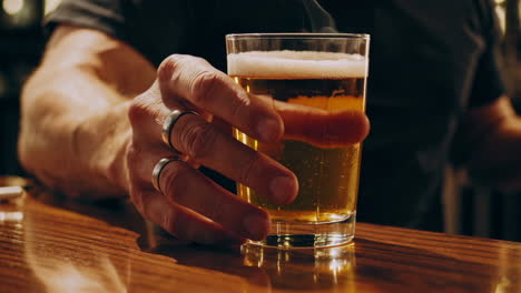 man holding a glass of beer at a bar