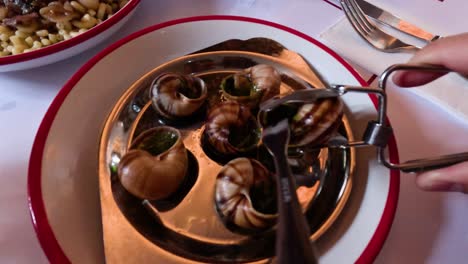 person using tongs to eat escargot