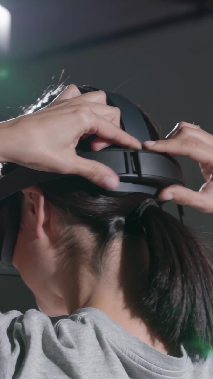 縦型動画：スタジオデモの準備をしているスウェットシャツ姿の女性が、クリップを調整しVRストラップをスライドさせている様子。