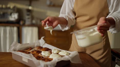 a baker frosting freshly baked cinnamon rolls