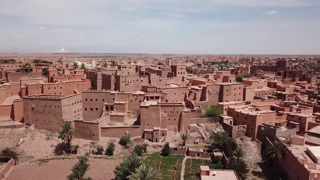 Ampia ripresa cinematografica con drone che cattura la vasta architettura in terra e le mura difensive di un tradizionale villaggio berbero fortificato nel deserto marocchino.