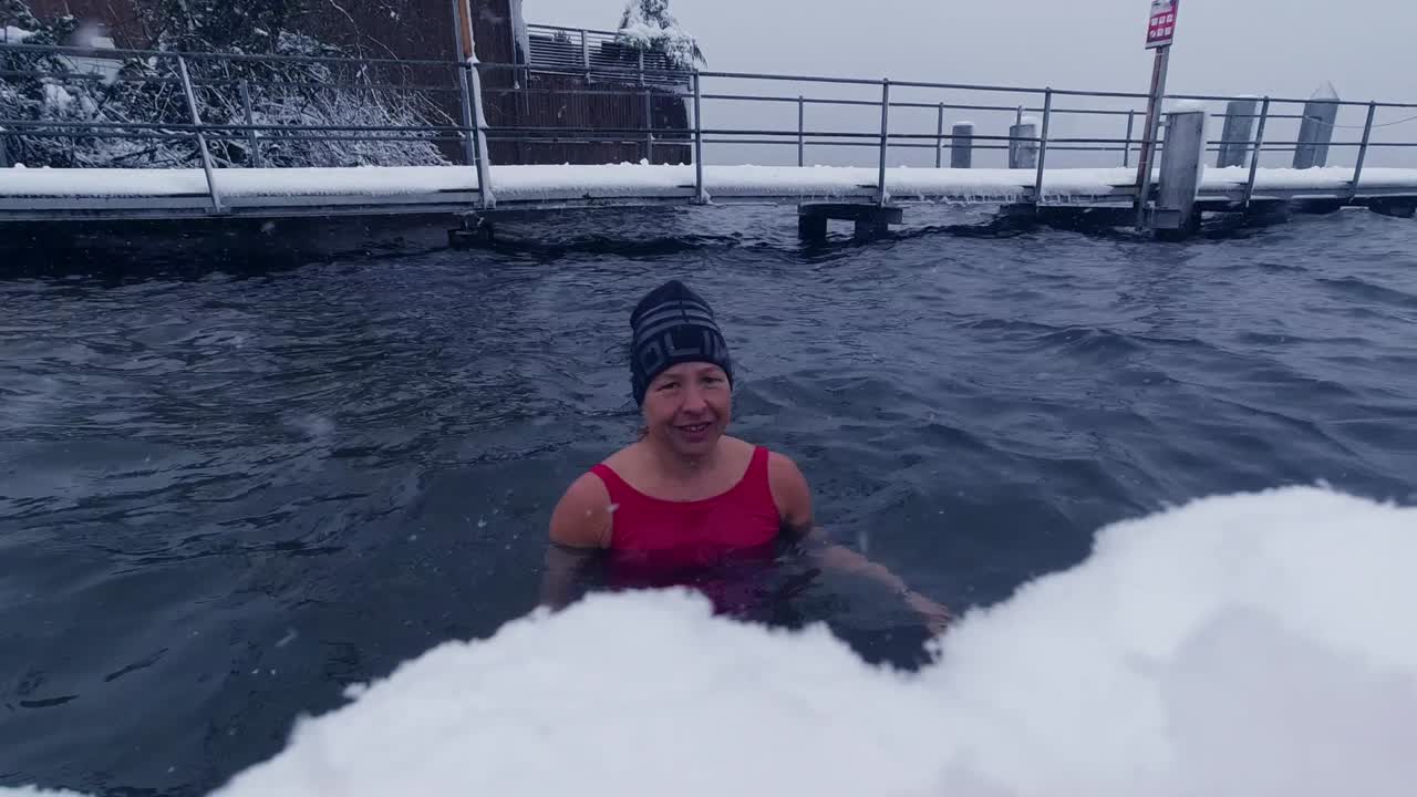 Halvbild av en kvinna som tar ett isbad i en schweizisk sjö under snöfall