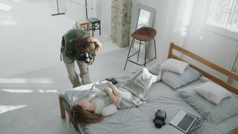 photographer capturing images of beautiful woman posing on bed in studio