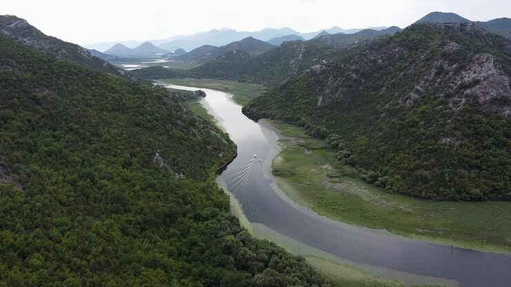 Una barca naviga lentamente sul fiume Crnojevica verso il lago di Skadar dal punto panoramico Pavlova Strana, Montenegro - Dolly aerea.