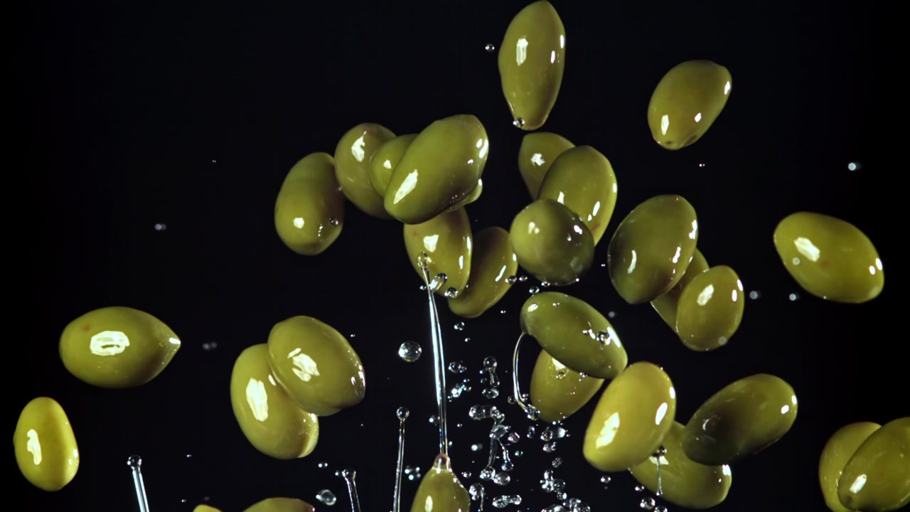Olive verdi fresche che cadono nell'acqua con schizzi al rallentatore.