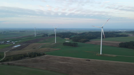 Large-Spinning-Windmills-Standing-On-Lush-Green-Field-In-Lubawa,-Poland---Drone-Shot