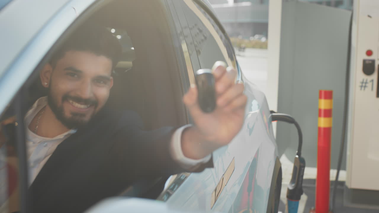 hombre sonriendo, sosteniendo la llave del coche en la estación de carga de vehículos eléctricos