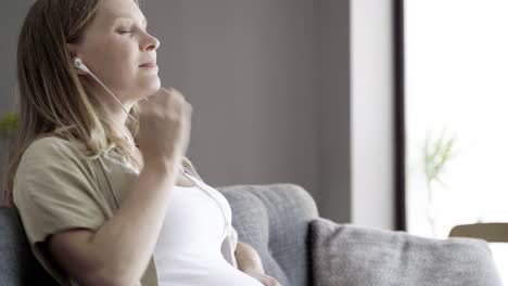 calm pregnant woman massaging belly and listening to music