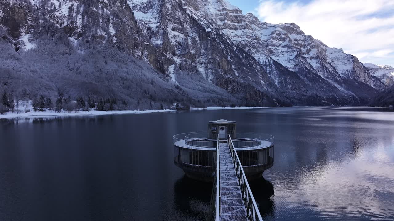 스위스 알프스 산맥의 한 겨울날에 탈레스 호수와 크래프트워크 탈 (kraftwerk klöntal) 위를 날아다니는 드론, 배경에는 vorderglärnisch 산과 vrenelisgärtli 산이 있습니다.