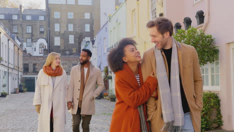 Multi-cultural-group-of-friends-hugging-as-they-walk-along-cobbled-mews-street-on-visit-to-city-in-autumn-or-winter---shot-in-slow-motion