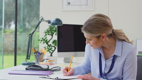 mujer médico o médico de cabecera en la oficina sentada en el escritorio escribiendo notas en el clipboard