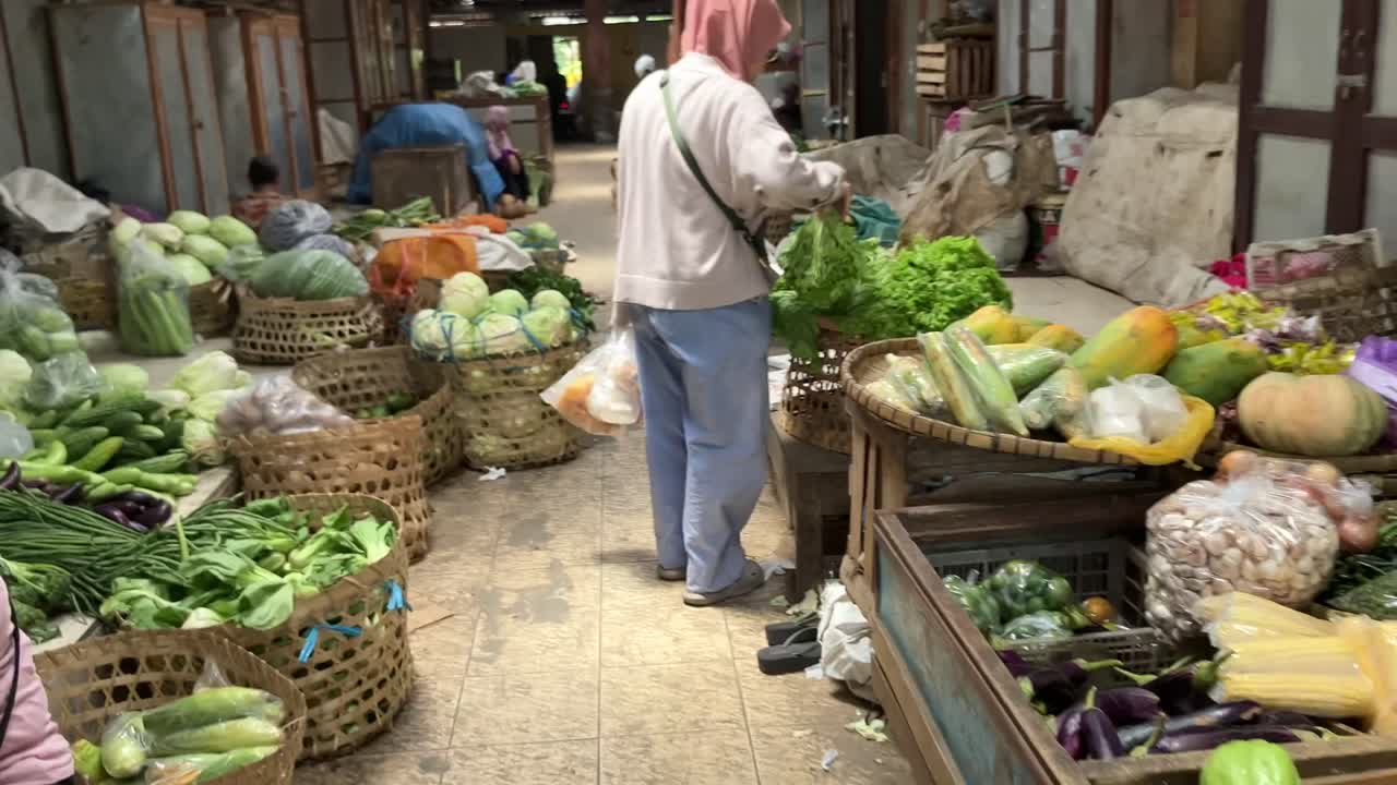 A woman wearing a hijab is buying organic vegetables sold by a vegetable trader at a traditional market.