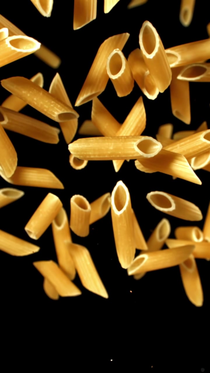 Pasta penne secca che cade al rallentatore su sfondo nero