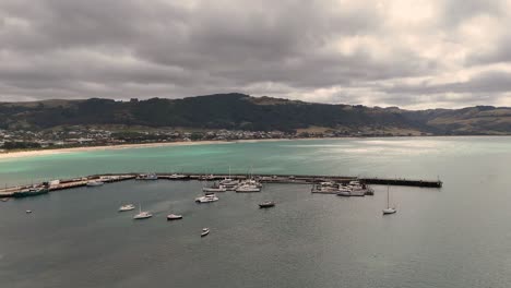 drone footage captures apollo bay harbor with boats under cloudy skies. calm waters and distant hills create a serene coastal scene