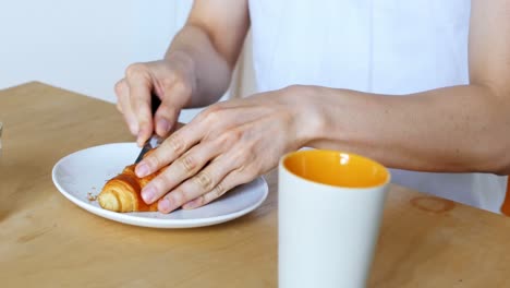 Man-slicing-croissant-with-knife-at-home-4k