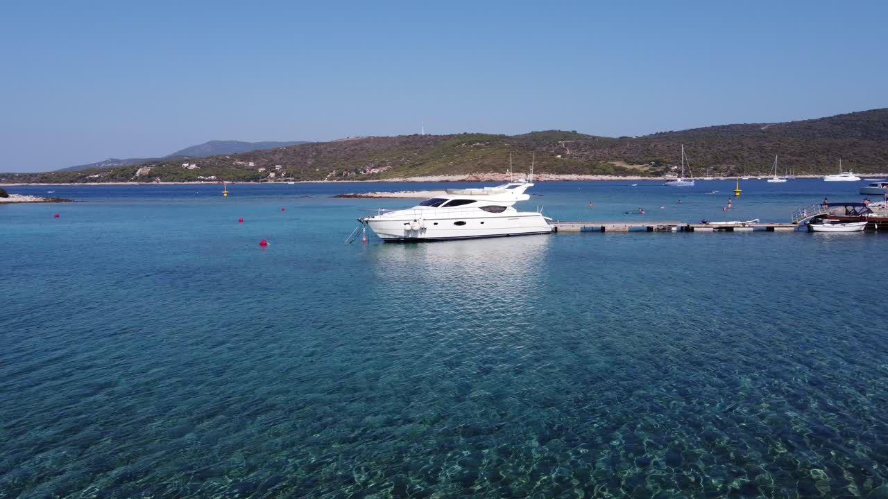 Giovane uomo che cammina in acqua bassa e uno yacht ormeggiato a un pontile di legno nella Laguna Blu, isola di Veliki Budikovac