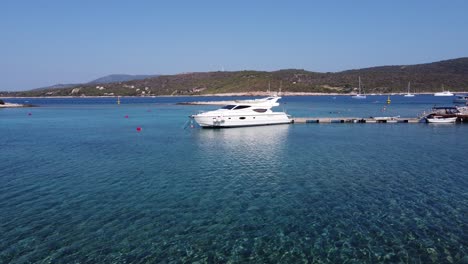 Young-man-walking-in-shallow-water-and-a-Yacht-boat-moored-to-wooden-jetty-dock-in-Blue-lagoon,-Veliki-Budikovac-island