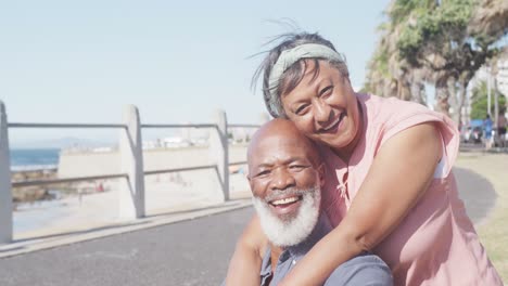 portrait of happy senior african american couple embracing on promenade by the sea, slow motion