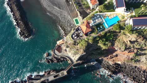 Disparo-De-Drones-Moviéndose-Hacia-Arriba-Lentamente,-Mirando-Hacia-Abajo-En-Un-Resort-De-Lujo-Sentado-En-La-Cima-Del-Acantilado-En-La-Costa-De-Madeira-Con-El-Océano-Durante-Una-Puesta-De-Sol