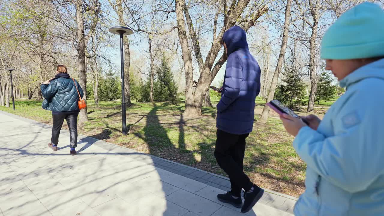 Menschen spazieren im Park und nutzen Smartphones an einem sonnigen Tag