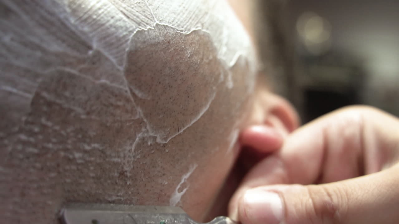 A close up shot of a razor blade shaving a beard gently, by a barber