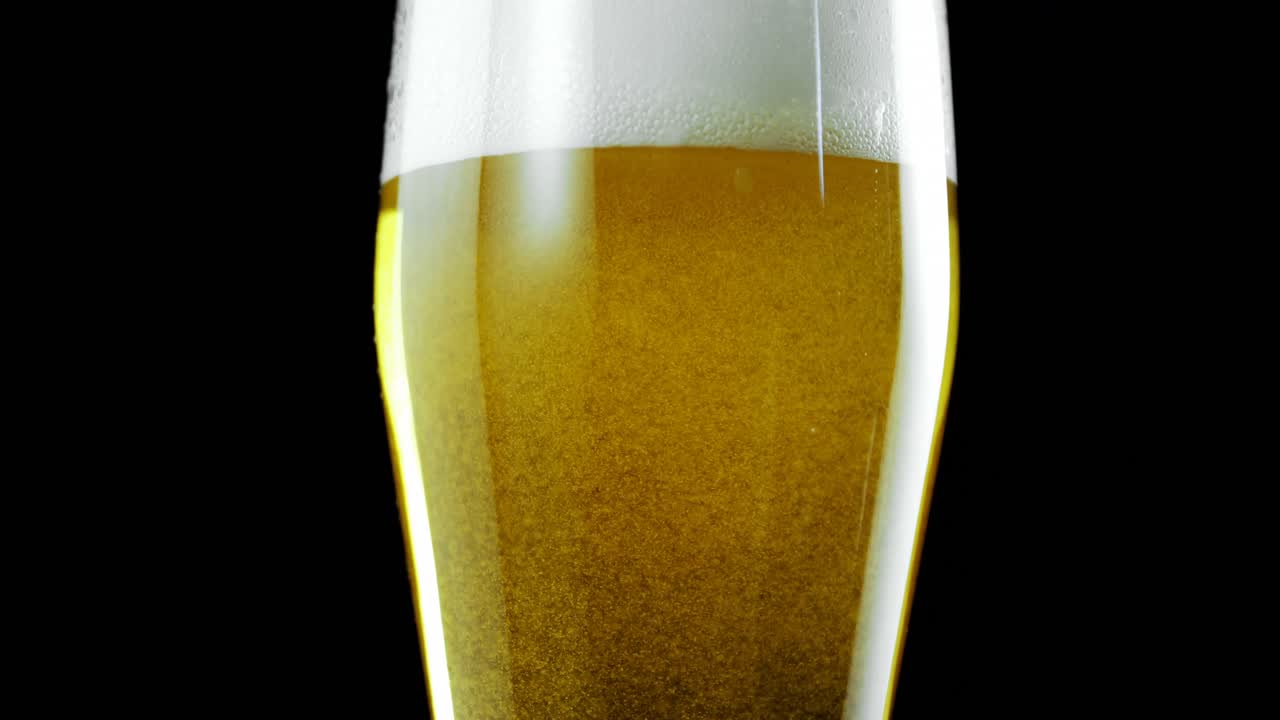 un vaso de cerveza contra un fondo negro 4k