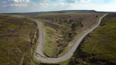 Aerial-video-showing-a-moorland-stream-flowing-under-a-small-bridge-then-through-a-wooded-ravine-towards-the-lower-ground