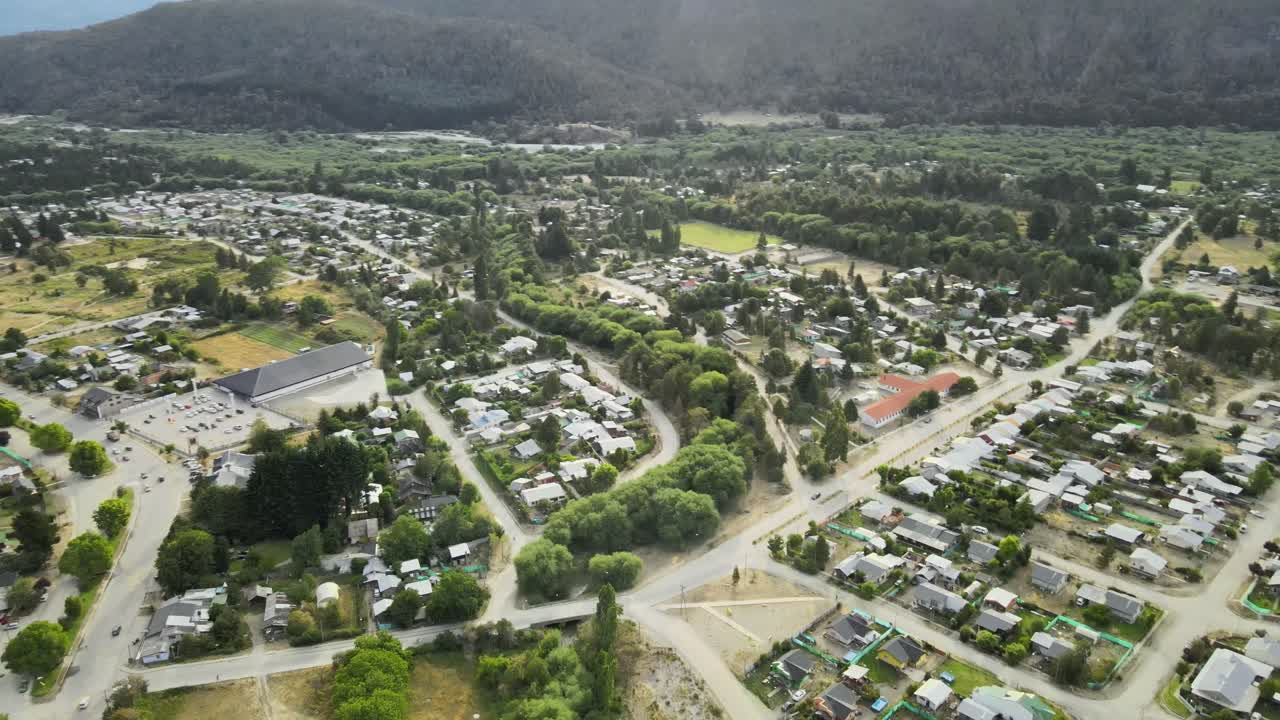 панорама слева, пролетающая над городом лаго пуэло, окруженным сосновым лесом, с озером и горными хребтами на заднем плане на закате, чубут, патагония аргентина
