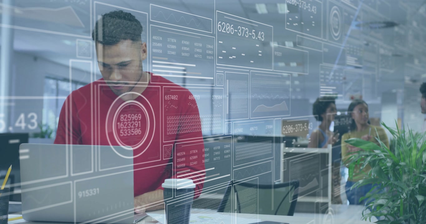 male data analyst typing on laptop in open-plan office, displaying floating holographic data panels