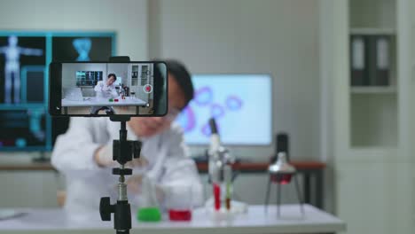 asian scientist man taking solution from test tube with micropipette putting in petri dish and using smartphone on tripod recording video