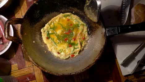 cooking delicious egg omelette in a hot pan with cooking oil in chinatown, bangkok, thailand - top view