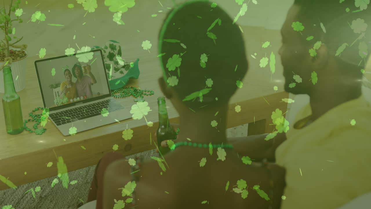 Clover leaves falling against couple holding beers having video call on laptop at home