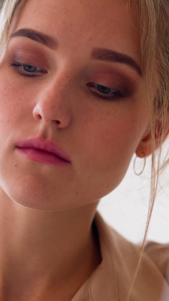 Focused young woman with fair hair locks and large eyes in beige shirt looks at screen of laptop working remotely at home slow motion extreme closeup
