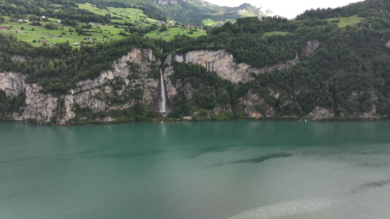 The Seerenbach Falls cascade down steep, forested cliffs and into the turquoise waters of Walensee in Switzerland. The view encompasses the dramatic alpine landscape near the towns of Amden, Betlis