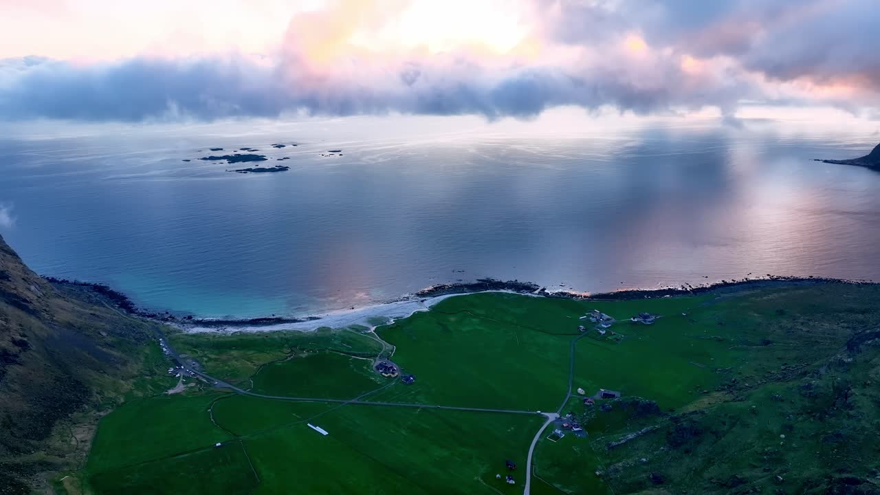 Golden pink midnight sun over Utakleiv beach as drone tilts slowly up from high altitude