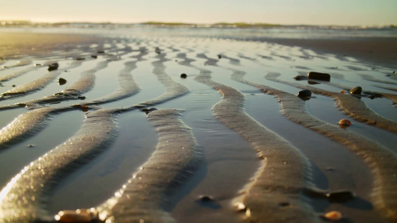 Landscape tidal flat shifting as gentle tide nudging thin pools rippled sand glinting under low sun