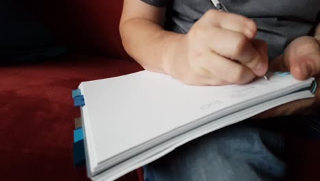 male with a partially amputated index finger on his right hand sat down holding a pen and pad  writing a to do list.