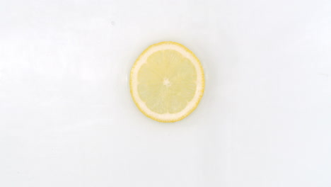 On-a-white-background-a-splash-of-water-falls-on-a-slice-of-lemon-in-slow-motion.