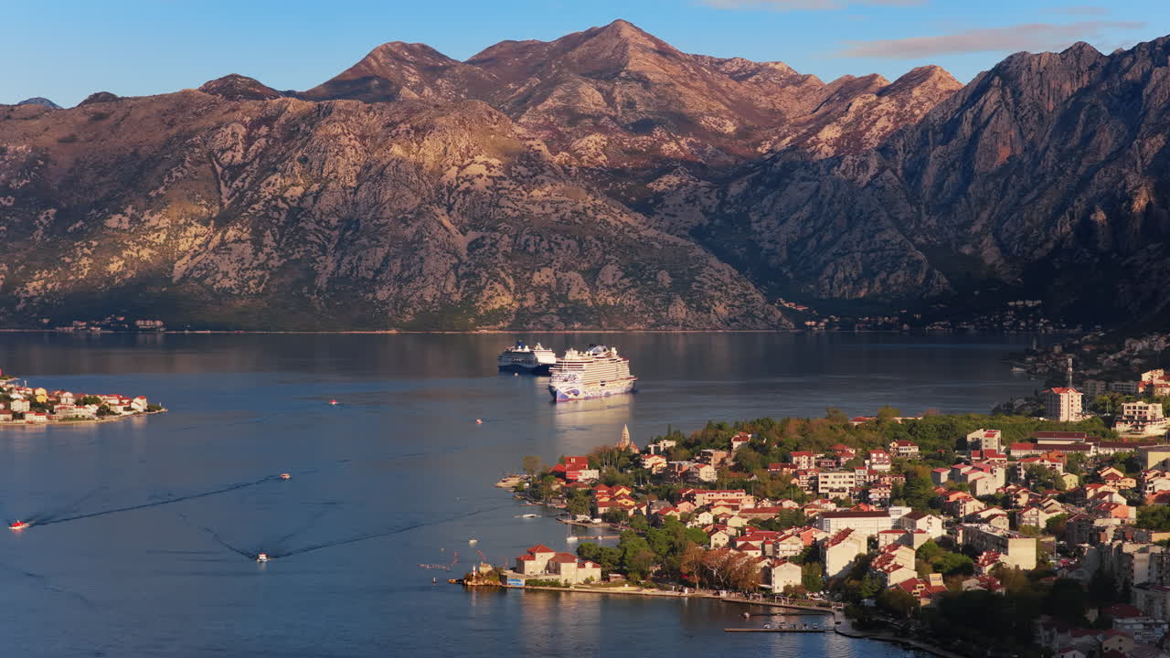 Aerial drone view of a cruise ship anchored in the Bay of Kotor with mountains glowing in soft light