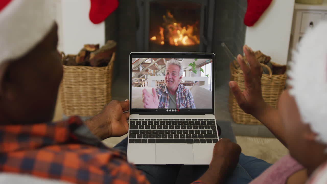 pareja afroamericana con sombreros de santa usando una computadora portátil para una videollamada de navidad con un hombre en la pantalla