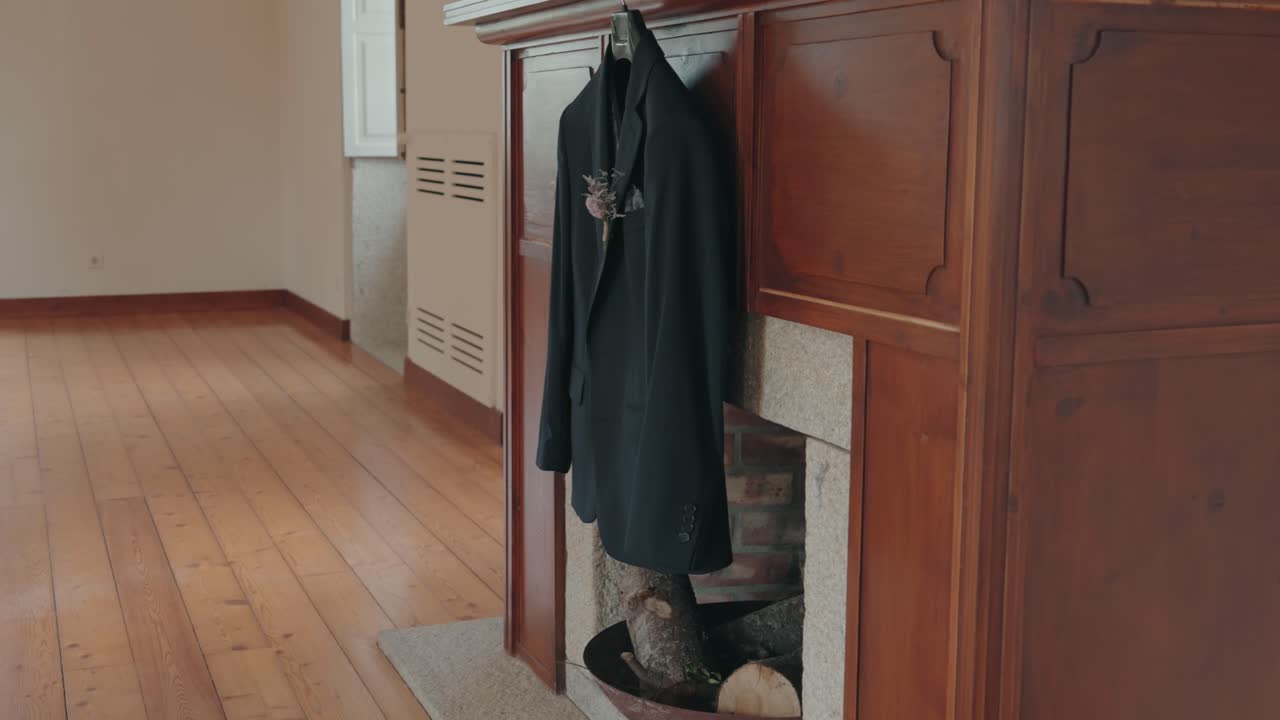 Dark wedding suit hanging near a wooden fireplace in soft warm light