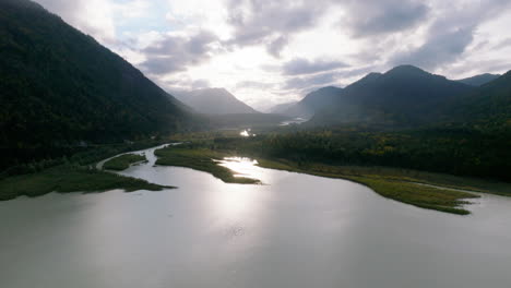 Vista-Aérea-Hacia-Adelante-Hacia-La-Luz-Del-Sol-Que-Se-Transmite-A-Través-De-Las-Brumosas-Colinas-Del-Bosque-De-Montaña-De-Baviera-Y-La-Orilla-Del-Lago-Sylvenstein