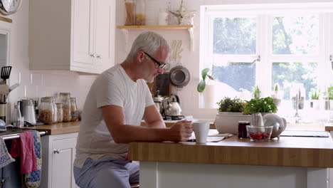 Mature-Man-In-Kitchen-Has-Breakfast-Whilst-Reading-Newspaper