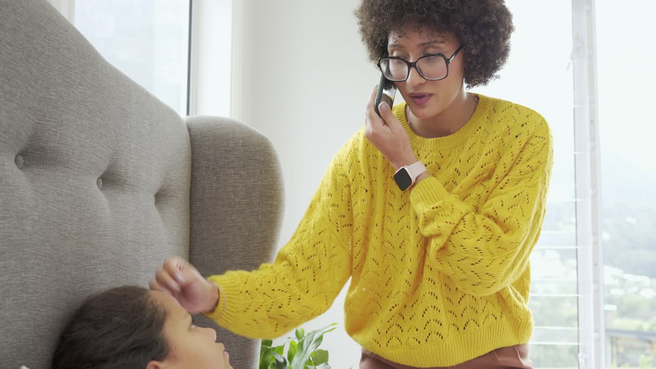 Mother and daughter taking phone call while checking her temperature and giving medicine at bedside