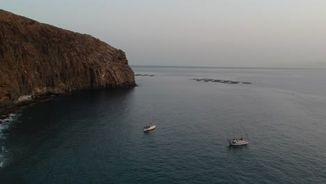 majestic rocky coastline of tenerife island with small boats, aerial descend view