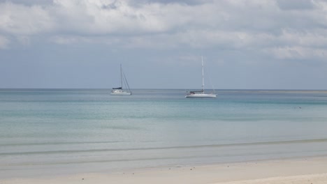 the beach with a few yachts in sea, white sand and wave from peaceful sea in sunshine daytime in phuket