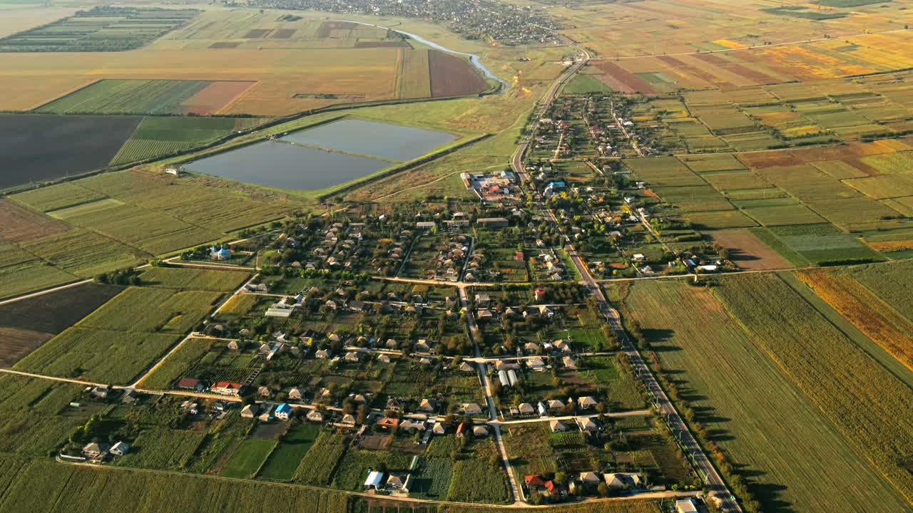 Aerial drone view of village in Moldova. Residential buildings, road with moving cars, lake, fields around