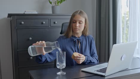 En-La-Oficina,-Una-Mujer-Vertiendo-Agua-De-Una-Jarra-De-Vidrio-En-Un-Vaso-Pequeño.